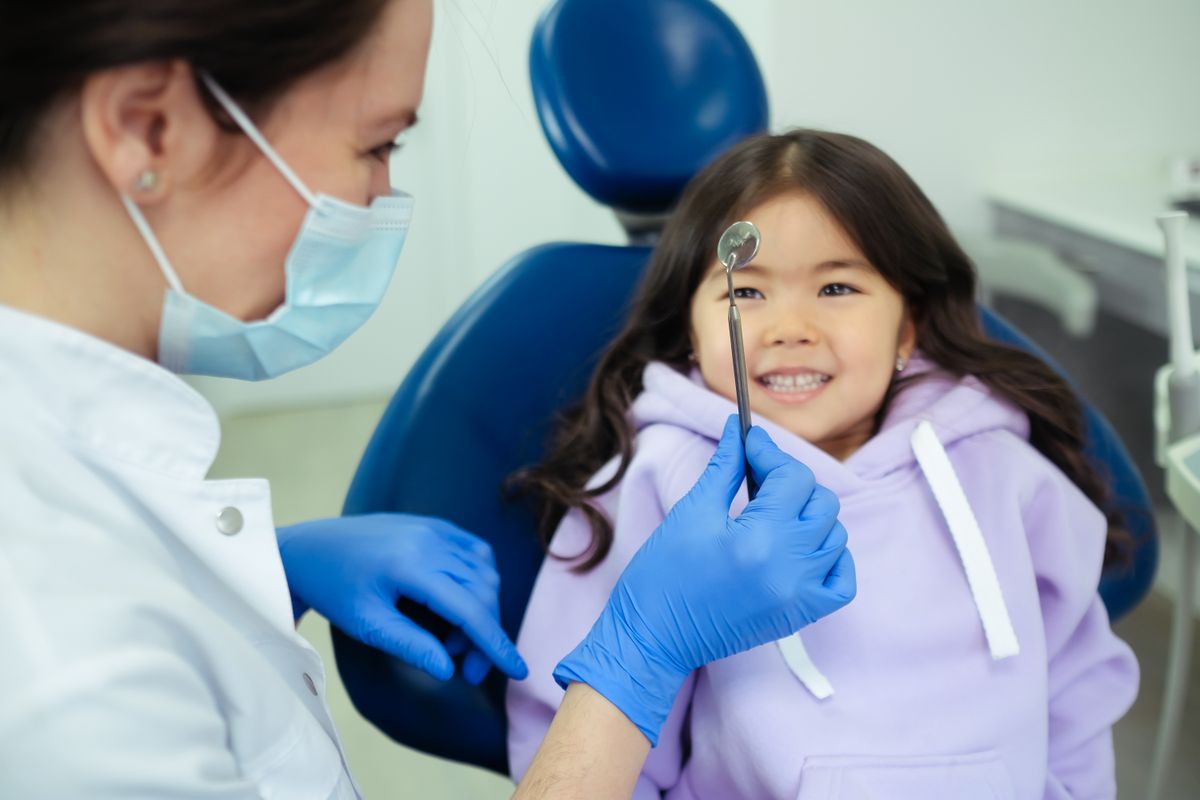 Dr. Priya showing a dental mirror to a smiling young patient in the treatment chair